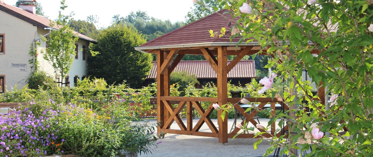 Von Büschen und Blumenhochbeet umgebener Holzpavillon mit Sitzgelegenheiten